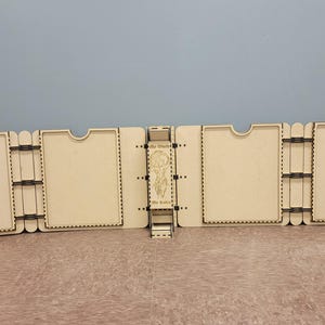 Könnte beinhalten: Ein hellbraunes Holzdisplay, bestehend aus mehreren durch Scharniere verbundenen Paneelen. Jedes Paneel hat eine rechteckige Form mit einer geschwungenen Oberseite und einem dekorativen, gepunkteten Rand. Das Display ist für den aufrechten Stand konzipiert.