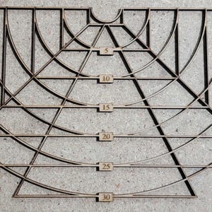 Peut inclure: Un motif géométrique en bois avec des lignes, des triangles et des arcs qui s'entrecroisent. Des marqueurs rectangulaires sont numérotés de 5 à 30. La forme générale évoque un éventail ou une arche stylisée.