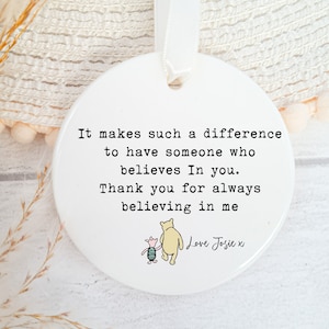 May include: White ceramic ornament featuring an illustration of Winnie the Pooh and Piglet. The ornament includes the text "It makes such a difference to have someone who believes in you. Thank you for always believing in me. Love Josie x".