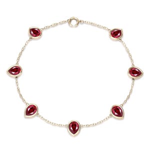 Può includere: Un delicato bracciale in argento con sette pietre preziose rosse a forma di goccia. Le pietre sono distanziate lungo una sottile catena, creando un design aggraziato. Il bracciale è assicurato da una piccola chiusura.