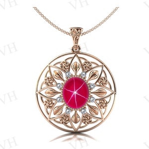 May include: A rose gold pendant necklace with a round, ornate frame featuring a red star ruby gemstone surrounded by smaller diamonds.