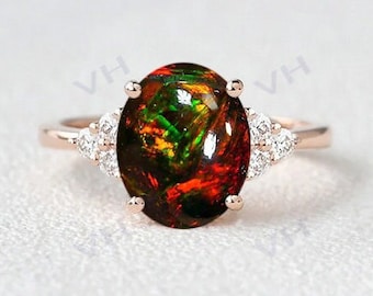 May include: A rose gold ring featuring a large oval opal gemstone, surrounded by smaller diamonds. The opal displays a vibrant mix of red, green, and black.