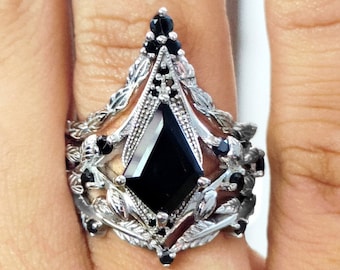 May include: A silver ring with a large black gemstone surrounded by smaller black gemstones and intricate silver designs.