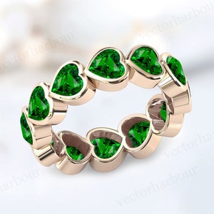 Puede incluir: Un anillo de banda de oro con una fila continua de piedras preciosas en forma de corazón verde esmeralda.