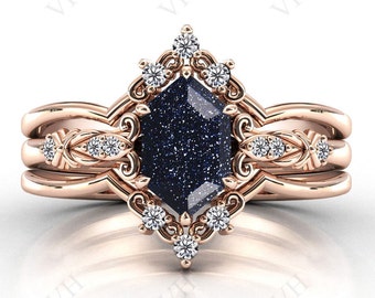 May include: A rose gold ring set with a large, dark blue, hexagonal gemstone surrounded by smaller, clear gemstones. The ring is set in a delicate, ornate design.