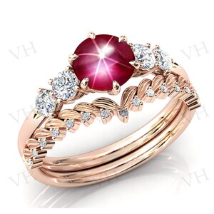 May include: A rose gold ring set with a large red star ruby and smaller white diamonds. The ring features a delicate floral design with leaves and small diamonds.