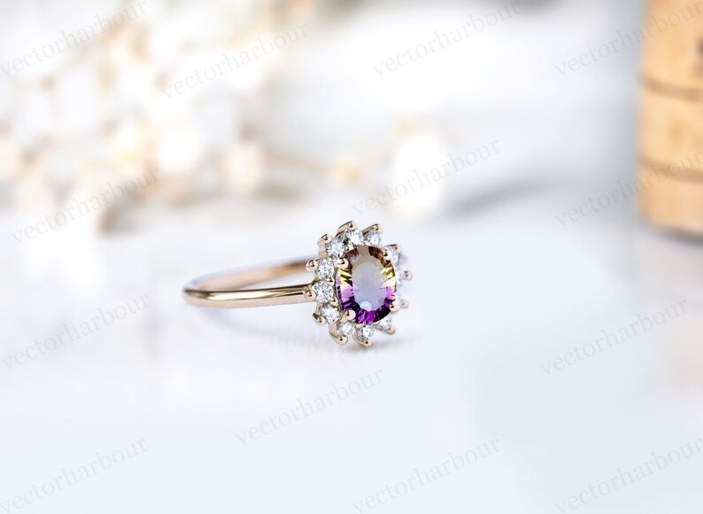 Puede incluir: Un anillo de oro con una piedra ovalada de color p&uacute;rpura y amarillo rodeada por un halo de diamantes m&aacute;s peque&ntilde;os.