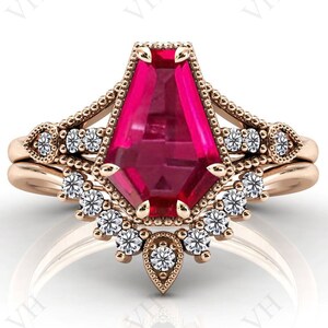 Puede incluir: Un anillo de compromiso de oro rosa con una gran piedra preciosa rosa facetada rodeada de piedras preciosas más pequeñas y transparentes. El anillo tiene un diseño delicado y ornamentado.