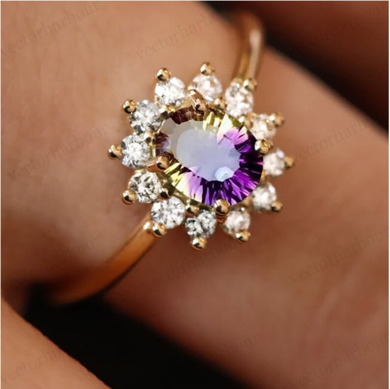Puede incluir: Un anillo de oro con una gran piedra preciosa ovalada que es una mezcla de verde, morado y amarillo. La piedra preciosa est&aacute; rodeada por un halo de piedras preciosas m&aacute;s peque&ntilde;as y transparentes.
