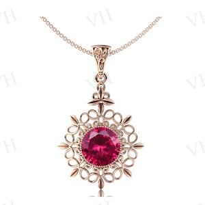 May include: A rose gold pendant necklace with a large, round, ruby-red gemstone. The gemstone is set in an ornate, openwork filigree design. The necklace chain is delicate and rose gold.