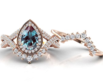 Könnte beinhalten: Ein Ring mit einem birnenförmigen blauen Edelstein, der von einem Heiligenschein aus kleineren Diamanten umgeben ist, der in eine Roségoldfassung gefasst ist. Der Ring wird mit einem passenden Roségoldband mit einer Reihe von Diamanten geliefert.