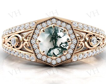 May include: A rose gold ring with a hexagonal setting featuring a green and white agate gemstone surrounded by a halo of smaller diamonds. The ring band is adorned with a delicate filigree design and a row of smaller diamonds.