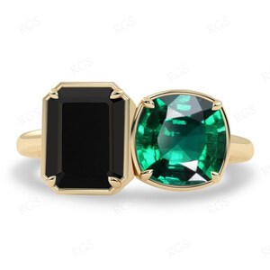 Puede incluir: Un anillo de oro con dos piedras preciosas. La piedra más grande es una esmeralda verde brillante, y la piedra más pequeña es un ónix negro.