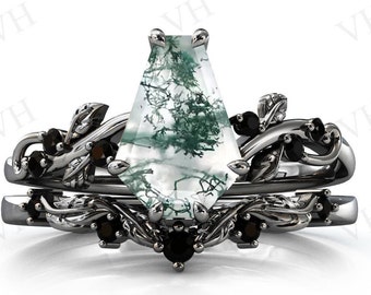 Op de afbeelding: Een zilveren ring met een grote, groen-witte mosagaten edelsteen. De ring heeft een delicaat, bladerig ontwerp met zwarte edelstenen.