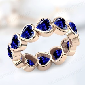 May include: A rose gold band ring with a continuous row of heart-shaped blue sapphires.