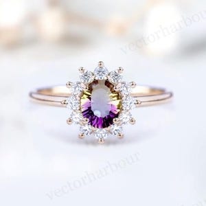 Puede incluir: Un anillo de compromiso de oro rosa con una gran piedra preciosa ovalada de color p&uacute;rpura y verde rodeada por un halo de diamantes m&aacute;s peque&ntilde;os.
