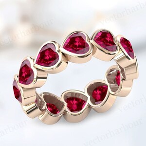 May include: A rose gold eternity band ring with a continuous row of heart-shaped ruby gemstones.