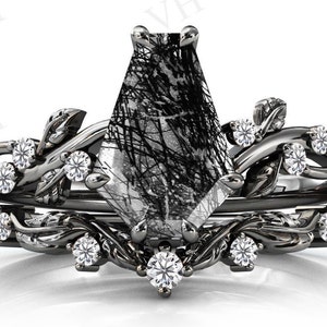 Puede incluir: Un anillo de piedra preciosa blanco y negro con un diseño único e intrincado. El anillo presenta una piedra preciosa grande, facetada, blanca y negra rodeada de piedras preciosas más pequeñas y transparentes. La banda es negra y presenta un delicado diseño de hojas.