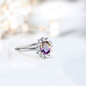Puede incluir: Un anillo de plata con una gran piedra preciosa ovalada que tiene un degradado de color p&uacute;rpura, amarillo y naranja. La piedra preciosa est&aacute; rodeada por un halo de piedras preciosas m&aacute;s peque&ntilde;as y transparentes.