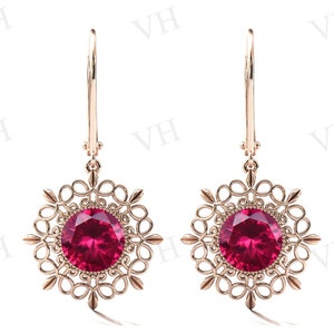 May include: A pair of rose gold earrings with a red gemstone set in a filigree design.