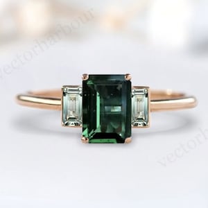 May include: A rose gold engagement ring with a green emerald-cut gemstone and two smaller emerald-cut diamonds on either side.