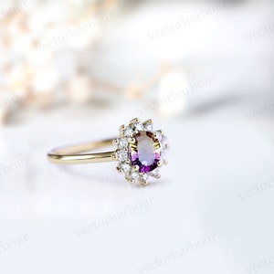 Puede incluir: Un anillo de compromiso de oro con una piedra ovalada de color p&uacute;rpura y amarillo rodeada por un halo de diamantes m&aacute;s peque&ntilde;os.