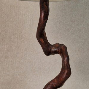 May include: A table lamp with a white fabric shade and a wooden base shaped like a twisted branch. The base is mounted on a flat, gray stone.