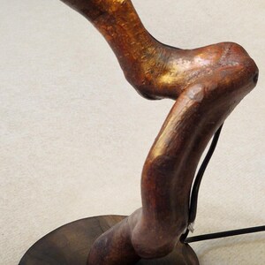 May include: A wooden lamp base with a natural wood finish and a dark brown wood base. The lamp base is shaped like a tree branch and has a gold metallic finish.