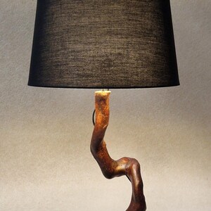 May include: A table lamp with a black fabric shade and a wooden base shaped like a twisted branch. The lamp has a black cord and a switch.
