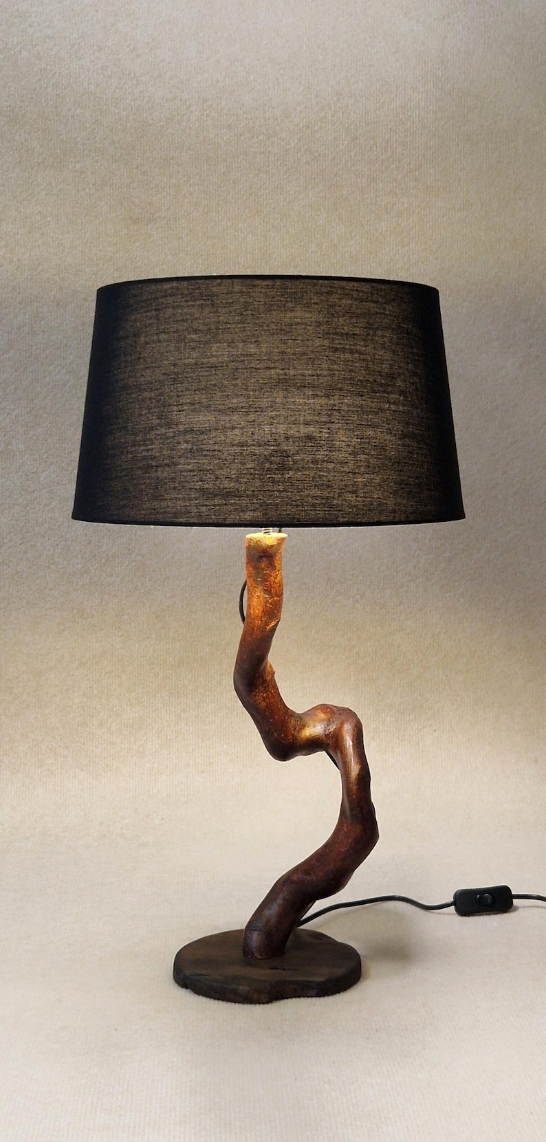 May include: A table lamp with a black fabric shade and a wooden base shaped like a twisted branch. The lamp has a black cord and a switch.