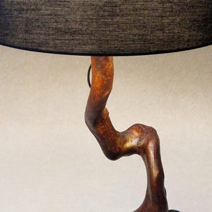 May include: A table lamp with a black fabric shade and a wooden base shaped like a twisted branch. The base is a dark brown color with a natural wood grain.