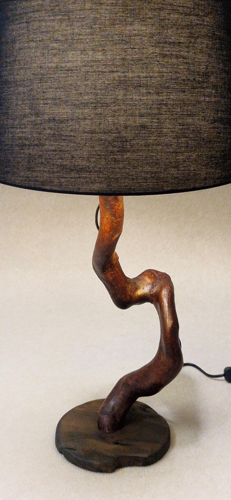 May include: A table lamp with a black fabric shade and a wooden base shaped like a twisted branch. The base is a dark brown color with a natural wood grain.