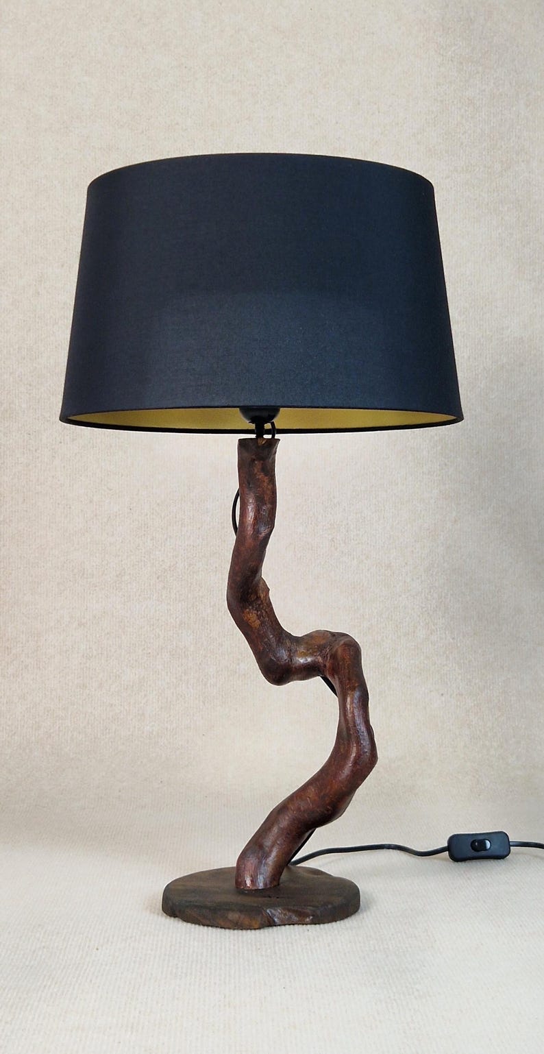 May include: A table lamp with a black fabric shade and a wooden base shaped like a tree branch. The base is dark brown and has a natural, rustic look.