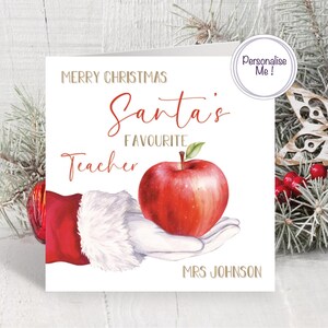 May include: A Christmas card with the text "Merry Christmas Santa's Favourite Teacher" and a watercolor illustration of an apple held in Santa's hand. The card includes the name "Mrs Johnson".