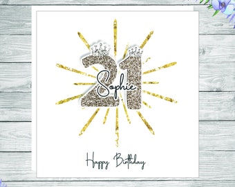May include: A square greeting card featuring the number 21 in a gold glitter texture, each digit topped with a small crown. The name Sophie is written in black script across the center, surrounded by gold sunburst rays and the text Happy Birthday.