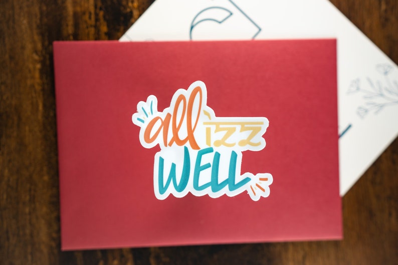 May include: A red envelope with a white sticker that says "all is well" in colourful lettering.