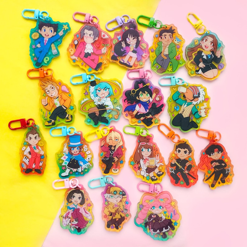 May include: A collection of 18 colorful keychains featuring cartoon characters. Each keychain is made of clear plastic with a glittery background and a colorful character design. The keychains are arranged in a grid pattern on a pink and yellow surface.