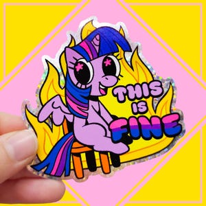 May include: A holographic sticker featuring a purple pony with a blue and pink mane sitting on an orange stool amidst yellow flames. The pony has large eyes with pink star-shaped pupils. The text THIS IS FINE is printed in bold letters.