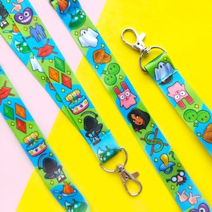 May include: Two colorful lanyards with various cartoon characters and designs. The lanyards are blue, green, and yellow with a white background. The lanyards have a metal clasp at the end.