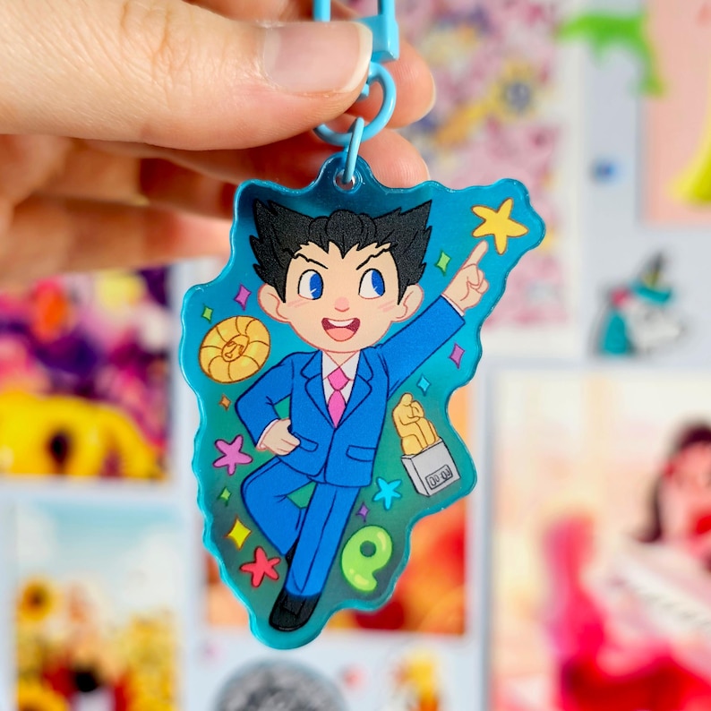 May include: A blue and white character keychain with a blue suit, pink tie, and a yellow star. The character is holding a box of food and pointing to the right. The keychain is made of clear acrylic and has a blue and white swirl pattern.