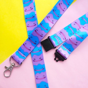 May include: Two purple and blue patterned lanyards with a silver clip and black plastic clasps. The pattern features a cartoon character with a smiling face.