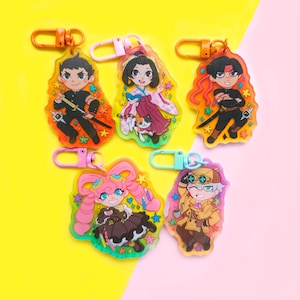 May include: Five colorful keychains featuring anime-style characters. Each keychain has a different character with a unique design and a colorful background. The keychains are made of clear acrylic and have a metal ring for attaching to keys or bags.