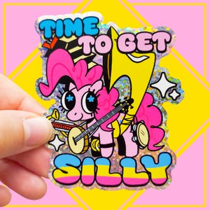 May include: A holographic sticker featuring a pink cartoon pony playing a banjo and a harmonica, with a large yellow tuba behind it. The text reads TIME TO GET SILLY in blue, pink, and yellow letters. The sticker has a sparkling, reflective finish.