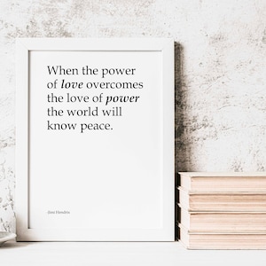 Op de afbeelding: Een wit ingelijst print met een citaat over liefde en vrede: "Wanneer de kracht van liefde de liefde voor macht overwint, zal de wereld vrede kennen." - Jimi Hendrix.