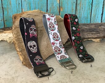 May include: Three keychains with different skull and floral designs. The keychains are black, white, and red with silver key rings. The keychains are numbered 1, 2, and 3.