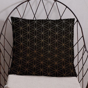 May include: A black throw pillow with a gold geometric pattern sits on a metal chair with a white cushion. The chair is in front of a white wall.