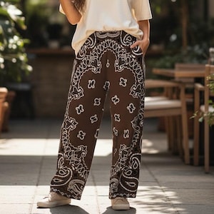 May include: A plain cream-colored short-sleeved t-shirt paired with loose-fitting brown trousers featuring a white paisley and floral bandana-style print. The trousers have a high-waisted design with side pockets and a wide-leg silhouette.