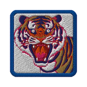 May include: Embroidered patch featuring a roaring tiger's head. The tiger has orange, navy blue, white, and pink details. The patch is square with a blue border and a white background.