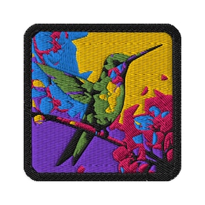 May include: Embroidered patch featuring a colorful hummingbird perched on a branch. The bird is depicted in shades of green, with a long black beak. The background includes yellow, blue, and purple hues, with pink flowers. The patch has a black border.