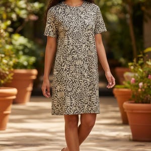 May include: A knee-length shift dress featuring a crew neckline and short sleeves. The garment is decorated with an intricate, repeating botanical pattern in cream against a dark olive green background, creating a consistent visual texture.